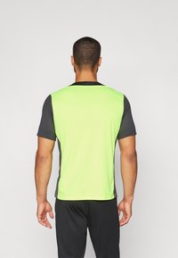 Camiseta atlética de manga corta con un frente de color verde brillante y una parte posterior gris oscuro. La tela parece ligera y con una textura suave.