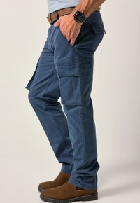 Modré cargo kalhoty se bočními kapsami, vyrobené z textura čtyřnásobného materiálu. Nosit s hnědým páskem a hnědými kotníkovými botami.