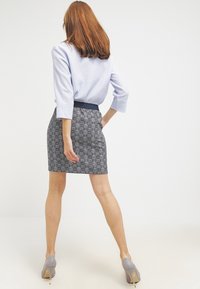 Top azul claro con mangas hasta el codo, combinado con una falda oscura con estampado. La modelo lleva tacones grises de punta puntiaguda.