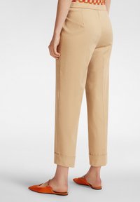 Pantaloni beige su misura con risvolti, caratterizzati da una texture liscia. Abbinati a scarpe slip-on arancioni con un design a punta.