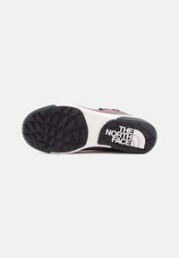 Potplat tenisice s crnim teksturiranim gumenim uzorkom, bijelim međupotplatom i logotipom The North Face ispisanim u bijeloj boji.
