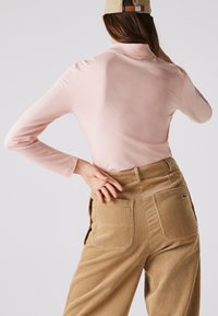 Rožinė ilgomis rankovėmis polo marškinėliai derinami su smėlio spalvos kordūrinių kelnių, turinčių vertikalias juosteles ir dvi užpakalines kišenes. Kepurė dėvima atvirkščiai.