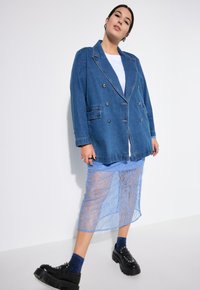 Blazer de mezclilla oversize en azul oscuro con botones de doble pecho, combinado con una falda de encaje azul claro y zapatos de plataforma negros gruesos.