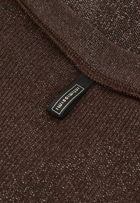 Nahaufnahme von dunkelbraunem, strukturiertem Strickstoff mit einem schwarzen, eingestickten Etikett, auf dem "Intimissimi" steht, das nahe dem Rand angenäht ist.