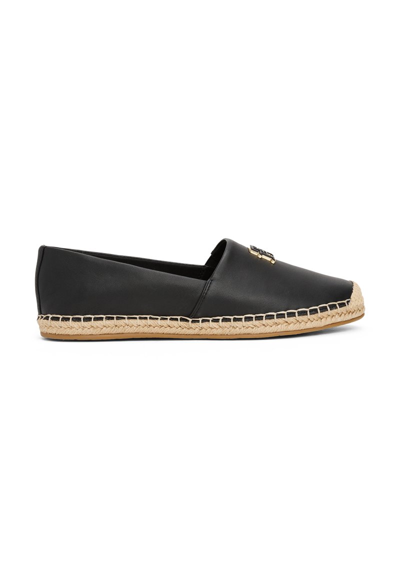 Espadrille en cuir noir avec un bord en jute naturel, design enfiler et un détail en emblème doré sur le dessus. Semelle plate, texture lisse.