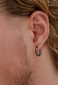 Sort metal hoops ørehængere set tæt på et øre. Ørehængeren har en glat, blank overflade og et cirkulært design.