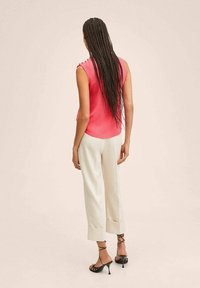 Rosa ärmelloses Top mit glatter Textur, kombiniert mit hellfarbenen, maßgeschneiderten Hosen und schwarzen Riemchen-High-Heels; minimalistisches Design, keine Muster.