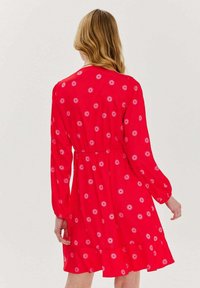 Červené šaty do délky kolen s dlouhými rukávy, elastickým pasem a květinovým vzorem. Vybavené vrstveným volánkovým lemem pro přidaný detail.