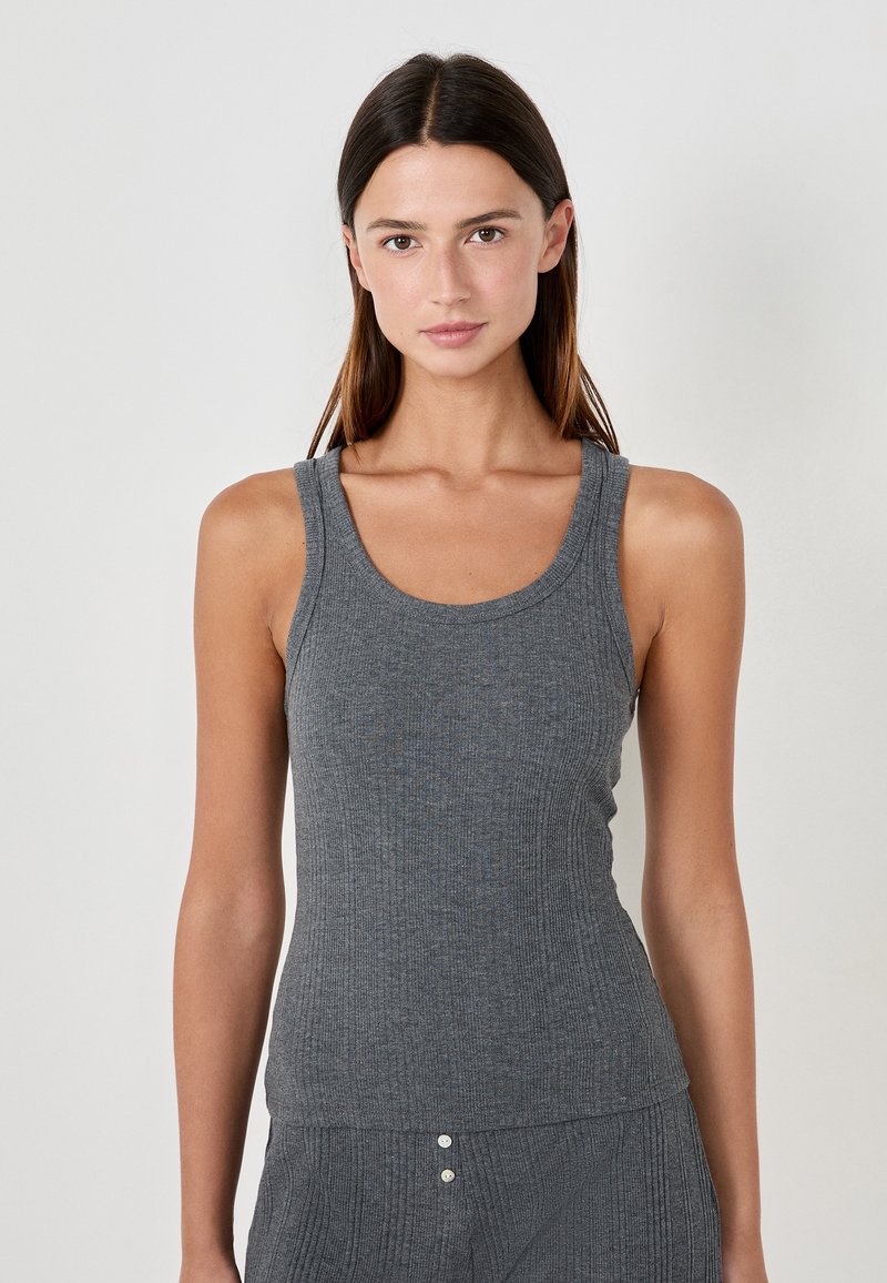 Top sin mangas de color gris con canalé, con tirantes anchos y un escote redondeado, presenta un diseño ajustado y una textura sutil, combinado con pantalones a juego.