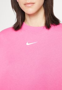 Detailní záběr na osobu v jasně růžovém svetru Nike s bílým logem Nike swoosh na hrudi.