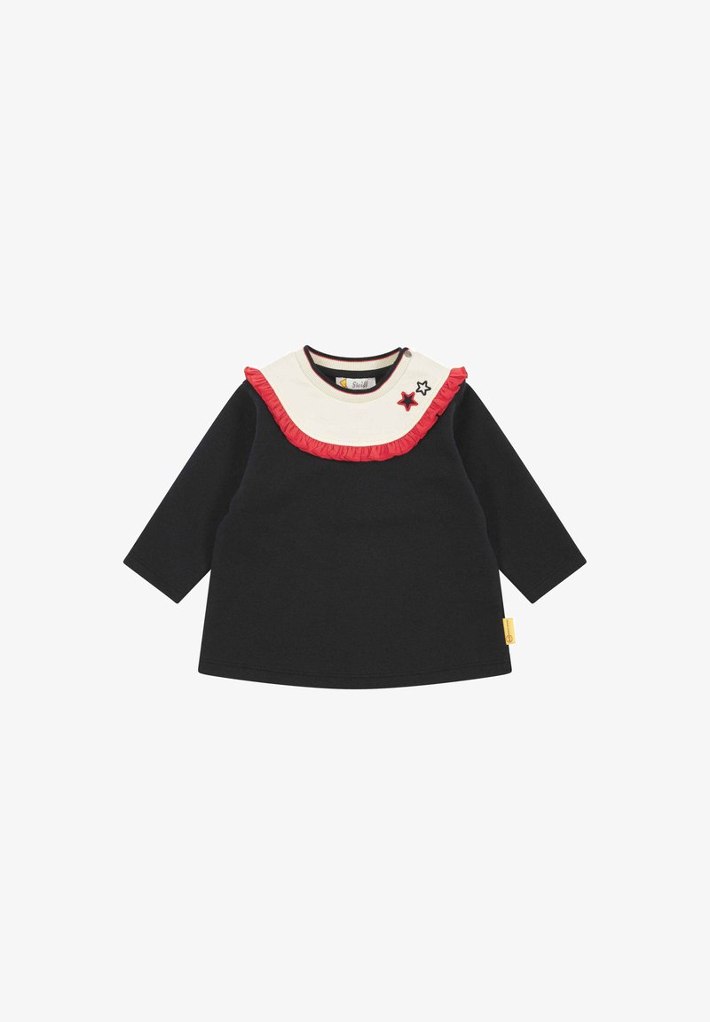 Zwarte langemouwen top met een crèmekleurige ruche-kraag, rode accenten en geborduurde sterdetails. Katoenen stof met een relaxte pasvorm. Gekleed aan de zijkant.