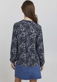 Blusa navy con motivo astratto a macchie bianche, maniche lunghe e orlo arrotondato. Abbinata a una gonna in denim, caratterizzata da un design classico.