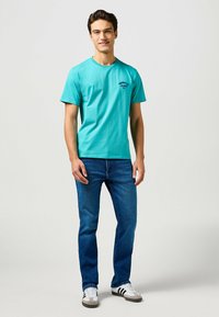 Cyan katoen T-shirt met korte mouwen en een ronde hals, gecombineerd met blauwe denim jeans en grijs-zwarte sneakers.