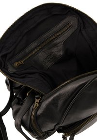 Zwarte leren tas interieur met een ritszak. Heeft een gladde textuur en gouden rits hardware op een zwarte voering.