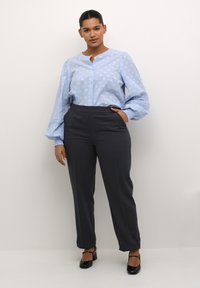 Helle blau, strukturierte Bluse mit Puffärmeln und Knopfleiste, kombiniert mit hoch taillierten, dunkelgrauen Hosen und schwarzen High-Heels.