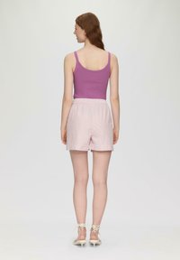 Lila gerippter Tanktop, hellrosa gestreifte Shorts mit elastischem Bund und beigefarbene High-Heel-Sandalen. Modell von hinten gezeigt.