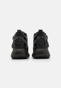 Adidași negri cu un superior texturat din piele și plasă, cu accente florale pe laterale și tălpi căptușite cu branding pe spate.