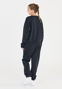 Mörk marinblå sweatshirt och matchande joggers tillverkade i mjukt tyg. Sweatshirten har en avslappnad passform och ribbade ärmmuddar. Byxorna har elastiska muddar.