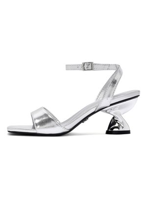 Sandalo argento con punta aperta, cinturino alla caviglia e tacco moderno scolpito di altezza media su sfondo bianco.