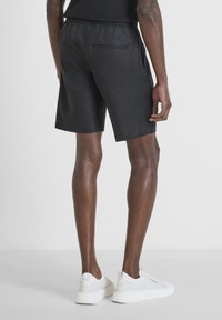 Pantaloni corti in lino neri con una cintura elastica, dotati di due tasche posteriori. Indossati con sneakers bianche, che mostrano uno stile casual e confortevole.