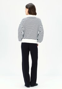 Maglione a righe bianco e navy, con una vestibilità ampia e maniche a palloncino, abbinato a pantaloni dritti navy e scarpe nere.