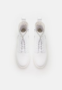 Bottes chelsea blanches en cuir avec une surface texturée, dotées de lacets et d'une fermeture éclair sur le côté. Design minimaliste avec un bout arrondi et une languette d'enfilage.