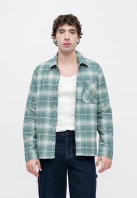 Πράσινο πουκάμισο με καρό μοτίβο σε απαλό ύφασμα με λευκές λεπτομέρειες, με κουμπιά μπροστά, μία τσέπη στο στήθος και άνετη εφαρμογή.