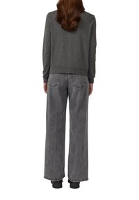Grijze trui met geribbelde manchetten en zoom, gecombineerd met brede, high-waisted zwarte jeans met subtiele stiksels en een onafgewerkte zoom.