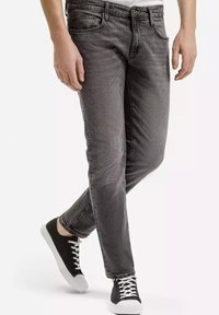 Szare dżinsy o slim fit, pięciu kieszeniach i delikatnym przetarciu. W połączeniu z czarnymi trampkami z białymi podeszwami i sznurówkami.