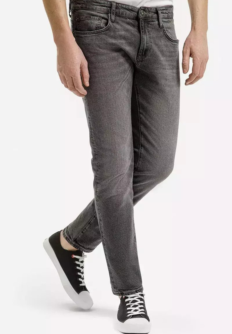 Szare dżinsy o slim fit, pięciu kieszeniach i delikatnym przetarciu. W połączeniu z czarnymi trampkami z białymi podeszwami i sznurówkami.