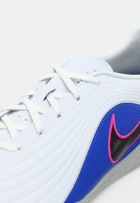 Λευκό αθλητικό παπούτσι με υφασμάτινη μπλε πλαϊνή επένδυση και μαύρο Swoosh περιγραμμένο με ροζ. Διαθέτει λευκά κορδόνια και γκρι σόλα.