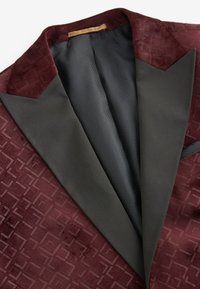 Veste de smoking bordeaux profond avec motif géométrique embossé et revers crantés en satin noir, montrée de l'intérieur et pliée à plat.