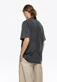 Camiseta de gran tamaño en gris oscuro con una textura suave, mangas cortas y cuello redondo, combinada con pantalones anchos beige. Sin detalles gráficos.