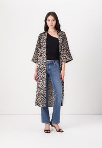 Robe in stile kimono con stampa leopardata e maniche ampie, realizzata in tessuto leggero; abbinata a un top nero e jeans blu. Sandali neri con tacco.