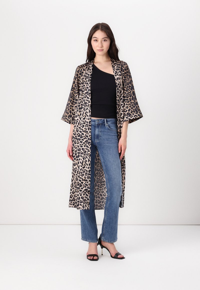 Robe in stile kimono con stampa leopardata e maniche ampie, realizzata in tessuto leggero; abbinata a un top nero e jeans blu. Sandali neri con tacco.