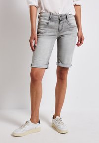Shorts en denim gris clair avec des revers roulés, dotés de poches avant, d'une fermeture à double bouton et d'une texture lisse. Associés à des baskets blanches.