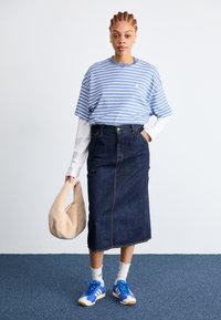 Maglietta a righe blu e bianca, lunga gonna di jeans scura, camicia bianca a maniche lunghe sotto, borsa beige, scarpe da ginnastica blu e calzini a fantasia.