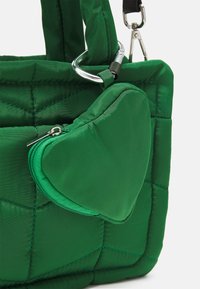 Sac à main en tissu matelassé vert avec des anses rembourrées, équipé d'une petite pochette triangulaire zippée attachée par un mousqueton argenté.