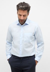 Lichtblauwe button-up shirt met een zak, lange mouwen en een netjes gestructureerde kraag, gecombineerd met donkere broeken. Gladde stoftextuur.