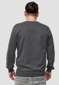 Sudadera gris de manga larga con puños acanalados. Diseño de cuello redondo y tejido texturizado, que presenta un detalle de costura redondeada en la parte trasera.
