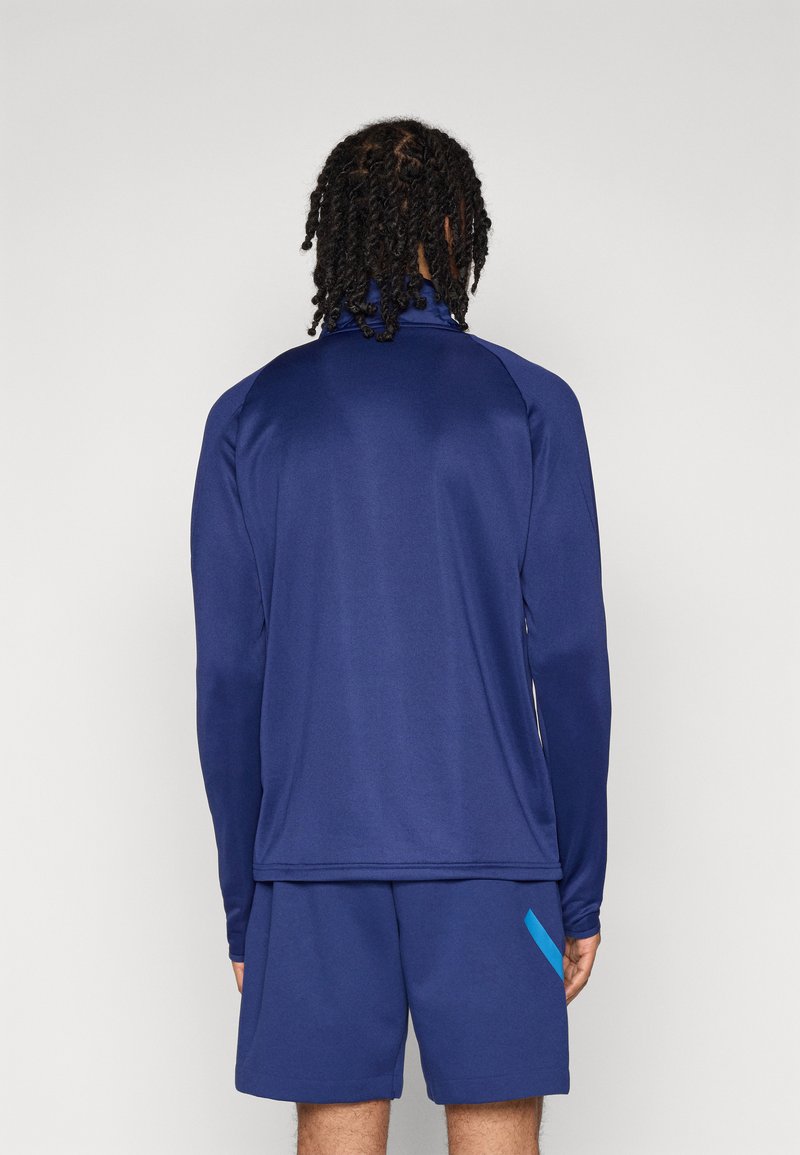 Haut de sport à manches longues bleu marine avec col montant, fabriqué en tissu lisse et léger ; associé à un short bleu marine avec une touche de bleu vif.