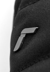 Tessuto nero con una piccola spilla nera opaca a forma di 'T' stilizzata, caratterizzata da una texture liscia e un design minimalista.