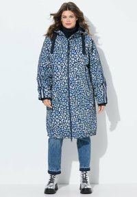 Zateplená parka s leopardím potiskem v modré barvě, se zapínáním na zip, s kapucí na stahování a bočními pruhy. Kombinována s džíny a stříbrnými botami na šněrování.