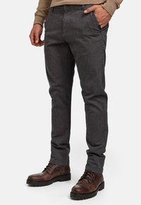 Pantalon gris à motifs avec une coupe slim, doté de poches latérales et d'une fermeture à bouton, associé à des bottes en cuir marron à lacets.