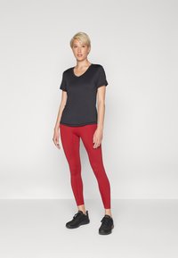 T-shirt noir à manches courtes et col en V, associé à des leggings rouges et des baskets noires. Tissu lisse, coupe ajustée et coutures minimales.