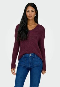 Maglione lavorato a maglia bordeaux con scollo a V e maniche lunghe, abbinato a jeans in denim blu a vita alta con tasche frontali e posteriori.
