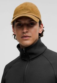 Giacca nera con zip e colletto alto, realizzata in tessuto liscio. Cappellino giallo con logo ricamato, realizzato in materiale morbido.