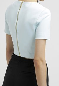 Light blue cropped top with short sleeves, featuring a gold zipper along the back. Smooth texture, fitted shape, minimalistic design.