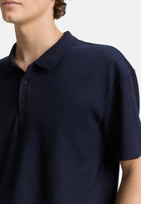 Navy-Polohemd aus strukturiertem Material, mit einem klassischen Kragen und einer Knopfleiste mit drei Knöpfen, entworfen mit kurzen Ärmeln.