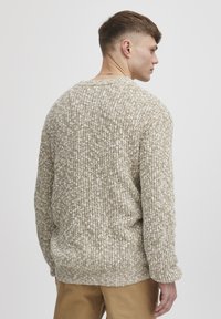 Knit sweater in beige and cream with textured pattern, wide crew neck, and long sleeves. Loose fit, shown from the back.